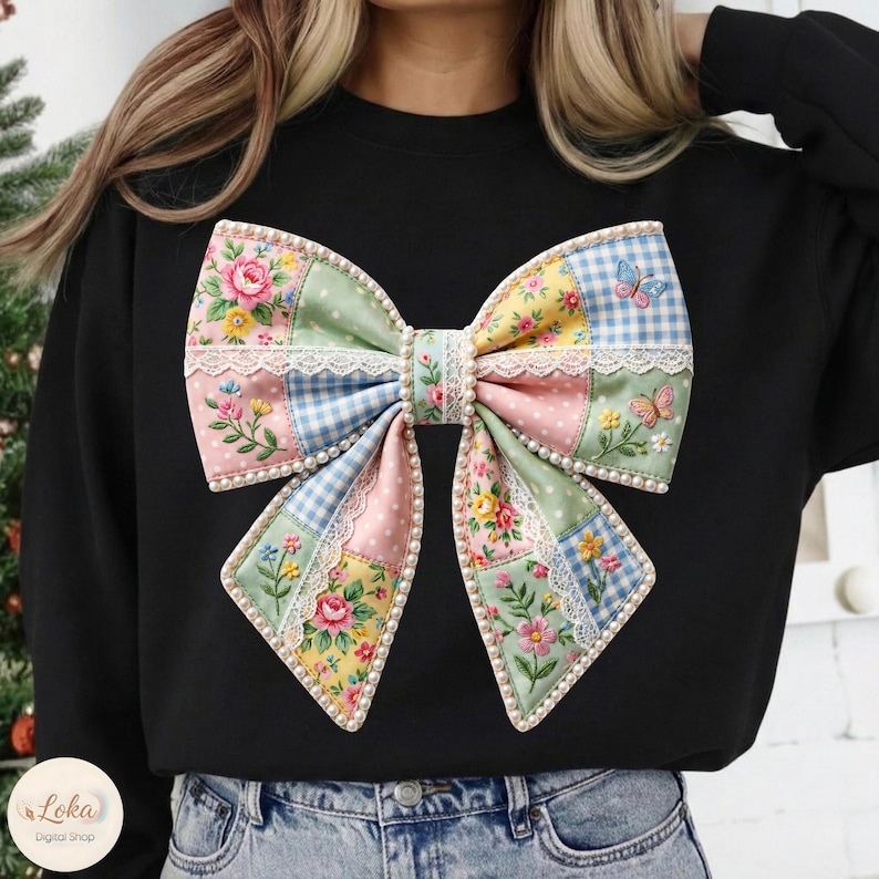 May include: Black sweatshirt featuring a large, colorful bow design. The bow is made of patchwork fabric with floral, polka dot, and gingham patterns. It is trimmed with lace and faux pearls, and has embroidered butterflies.