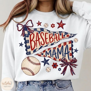 Puede incluir: Una sudadera blanca de manga larga con un estampado gráfico de dos banderines con el texto BASEBALL MAMA en rojo y azul. El diseño incluye una pelota de béisbol, lazos rojos y azules, estrellas y pequeñas flores en tonos patrióticos.