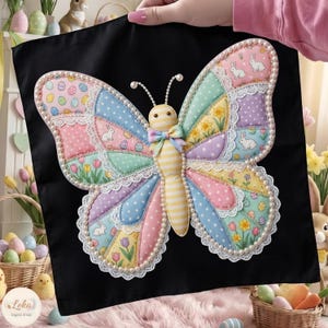 Puede incluir: Un cojín decorativo con forma de mariposa sobre un fondo negro. La mariposa tiene alas de patchwork pastel con diseños florales y de conejos, bordeadas con encaje blanco y perlas de imitación. El cuerpo de la mariposa es a rayas amarillas y blancas con un lazo.