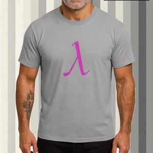 Könnte beinhalten: Graues T-Shirt mit einem magenta Lambda-Symbol. Das Shirt wird von einer Person getragen. Das Bild enthält den Text "JNJ UNITY RALEIGH, NC" und "LIVE LOUD. WEAR BOLD."