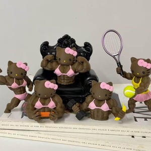 May include: A collection of five brown Hello Kitty figurines with muscular physiques, each wearing a pink bow. One sits on a black chair, while others hold a tennis racket, a yellow tennis ball, a dumbbell, a banana, and a small orange device.