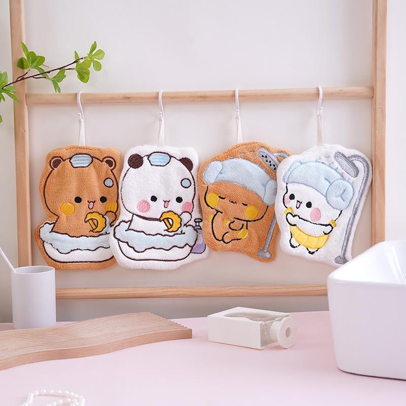 May include: Four plush washcloths with cartoon bear and panda designs, each with a unique bath-time theme. The washcloths are brown, white, and yellow, hanging on a wooden rack. Each cloth has a loop for hanging.