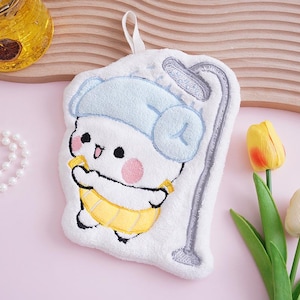 May include: White plush bath sponge with an embroidered cartoon character wearing a blue hat and yellow diaper. The sponge has a shower head design and a loop for hanging. The character has pink cheeks and is holding a yellow banana.