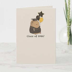 May include: Graduation greeting card featuring a cartoon character in a graduation gown and cap, holding balloons. The balloons are black and yellow. The card reads "Way to go!" and "Class of 2026!" on a cream background.