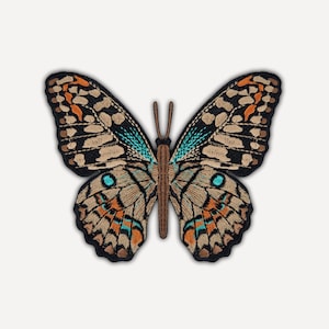 Può includere: Una toppa ricamata a forma di farfalla con corpo centrale e antenne marroni. Le ali presentano un motivo dettagliato nei toni del beige, nero, arancione brillante e blu turchese vivace, con un bordo esterno di colore nero.