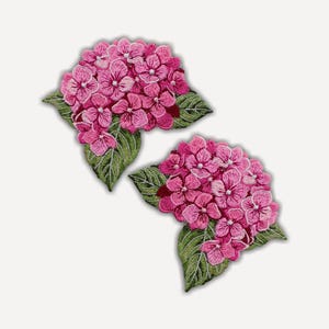May include: Two embroidered patches featuring clusters of vibrant pink hydrangea flowers with detailed green leaves. Each patch displays intricate stitching that captures the texture and layered petals of the blossoms and the veined foliage.