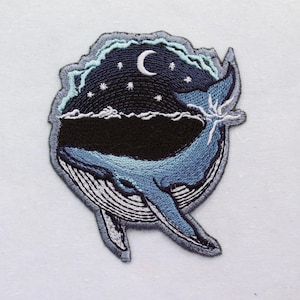 May include: Embroidered patch featuring a whale breaching the water under a night sky. The design includes a crescent moon, stars, and stylized waves. The whale is primarily blue with white accents, and the sky is dark blue with light blue details.