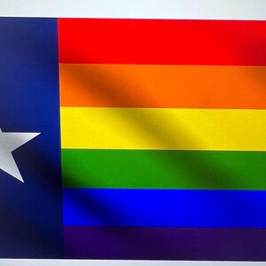 Puede incluir: Un diseño de bandera que combina la bandera del estado de Texas con los colores del arcoíris de la bandera del orgullo LGBTQ+. El lado izquierdo presenta el campo azul y la estrella blanca de la bandera de Texas, el lado derecho muestra las rayas del arcoíris.