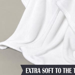 Pu&ograve; includere: Primo piano di una coperta bianca con tessuto morbido e fluido. La coperta &egrave; piegata, mostrando la trama e le cuciture lungo il bordo. Il testo in basso recita "EXTRA SOFT TO THE TOUCH."