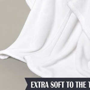 May include: Close-up of a white blanket with soft, flowing folds. The blanket has a smooth texture and is made of a plush material. The text "EXTRA SOFT TO THE TOUCH" is displayed at the bottom.