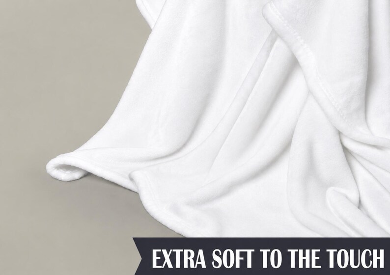 May include: Close-up of a white blanket with soft, flowing folds. The blanket has a smooth texture and is made of a plush material. The text "EXTRA SOFT TO THE TOUCH" is displayed at the bottom.