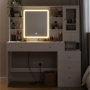 May include: A white vanity table with a lighted mirror, drawers, and shelves. The mirror has a rectangular shape with a glowing border. The vanity has gold-colored knobs and a small cabinet with drawers. A woven basket sits below the table.