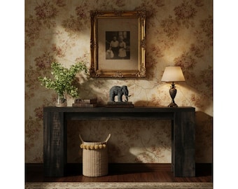 May include: A dark wood console table with a framed picture, a lamp, and a decorative elephant statue. A woven basket with yellow pom-poms sits below. The background features floral wallpaper and a vase of greenery.