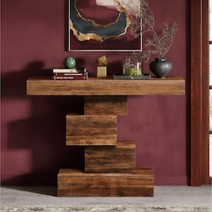 May include: A modern, wooden console table with a unique, stepped base design. The table is made of dark brown wood and has a rectangular top. Decorative items, including books, a vase, and a sculpture, are displayed on the table.