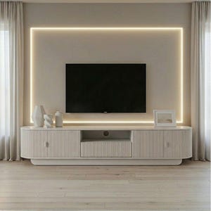 May include: A modern living room setup featuring a large black television mounted on a light-colored wall with a glowing rectangular border. Below, a matching white cabinet with vertical ribbed detailing houses storage and display space. Decorative vases and a framed picture add to the aesthetic.