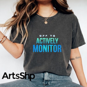 May include: Dark gray t-shirt with the text "OFF TO ACTIVELY MONITOR" in a gradient blue and green font. The shirt is a crew neck style and appears to be made of a soft material. The Etsy shop name "ArtsShp" is at the bottom.