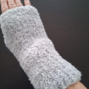 May include: A light gray, fluffy wrist warmer. The wrist warmer is made of a soft, textured material and covers the wrist and part of the forearm. The wrist warmer is designed to keep the wrist warm.