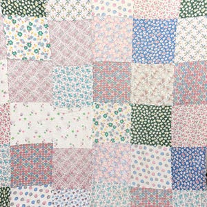 Può includere: Una trapunta patchwork composta da vari pannelli di tessuto quadrati con motivi diversi, tra cui stampe floreali, pois e quadri nelle tonalità del verde, blu, rosa e bianco, cuciti insieme in una struttura a griglia.