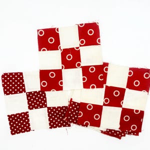 May include: Three square fabric quilt blocks arranged in a cluster. Each block features a nine-patch grid pattern alternating between solid off-white squares and red squares printed with white circles or white polka dots on a red background.