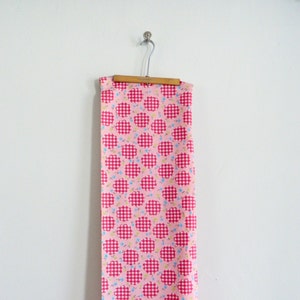 May include: Pink fabric with a white gingham pattern and small pink, blue, and yellow flowers. The fabric is hanging on a wooden hanger.