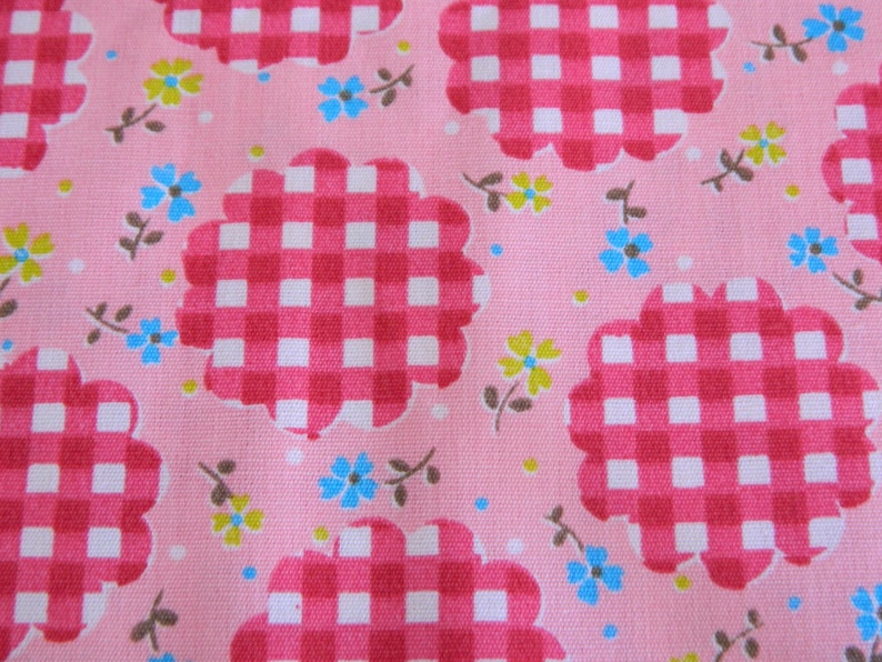 May include: Pink fabric with a repeating pattern of red and white gingham squares in a flower shape. The background is a light pink with small white dots and scattered blue and yellow flowers.