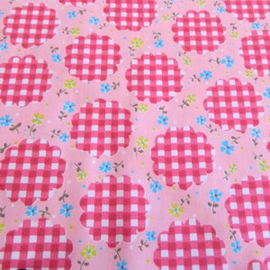 May include: Pink fabric with a repeating pattern of white and red gingham checkered flowers. The flowers have a scalloped edge.