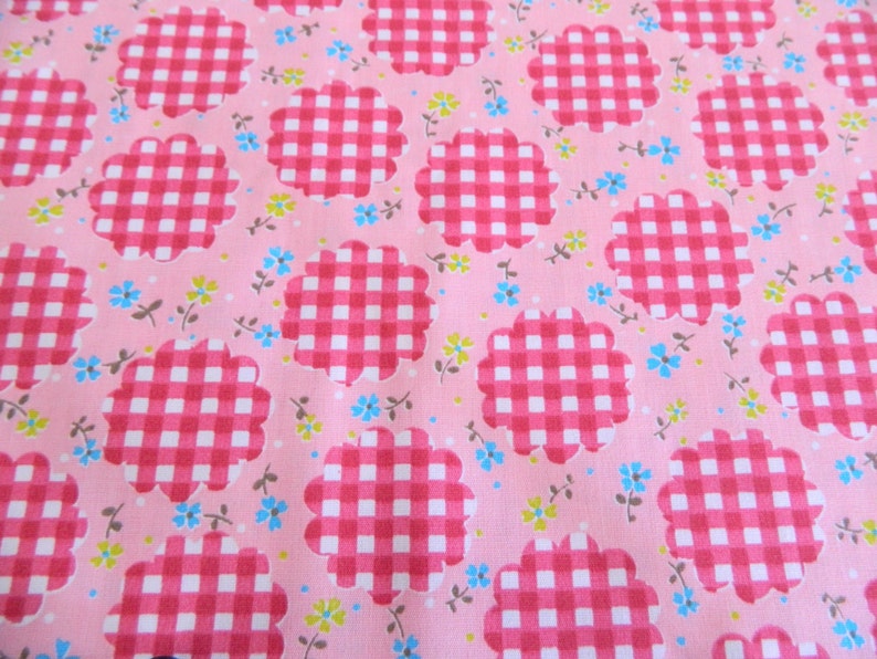 May include: Pink fabric with a repeating pattern of white and red gingham checkered flowers. The flowers have a scalloped edge.