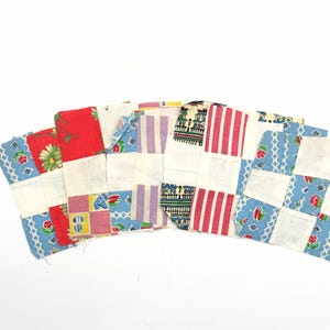 May include: A collection of rectangular fabric patches arranged in a fan shape. The patches feature various patterns including red and green floral prints, pink and white stripes, blue geometric designs, and small colourful motifs on white backgrounds.