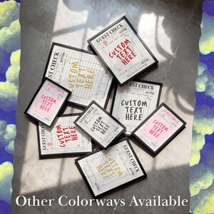 May include: An assortment of framed guest check prints with the text "CUSTOM TEXT HERE" in various colors, including red, pink, and gold. The prints are arranged on a light-colored surface, with the words "Other Colorways Available" at the bottom.