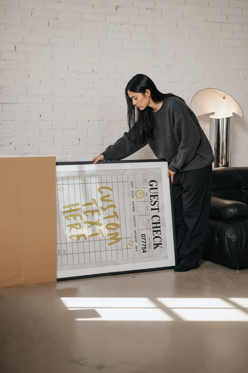 May include: A framed print with the words "CUSTOM TEXT HERE" in gold lettering. The print also includes a "GUEST CHECK" section with a grid and the number "077754". The frame is black.