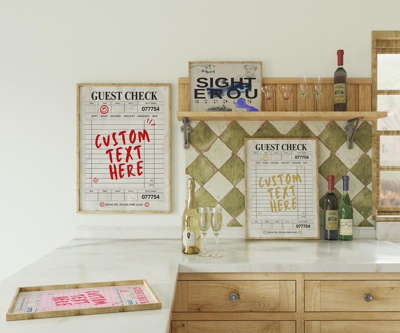 May include: A kitchen scene featuring framed "Guest Check" prints with "Custom Text Here" in red and yellow. Wine bottles, champagne, and glasses are arranged on a countertop and shelf. A wooden tray with a pink guest check is in the foreground.