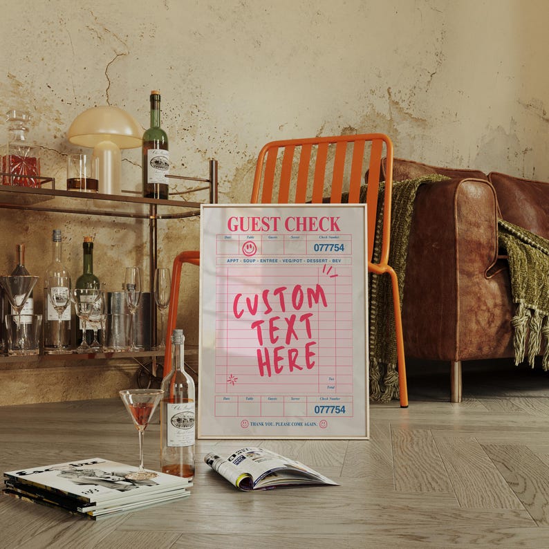May include: A framed "Guest Check" sign with pink grid lines and the words "Custom Text Here" in pink. The sign is propped up against an orange chair. A bar cart with bottles and glasses is in the background.