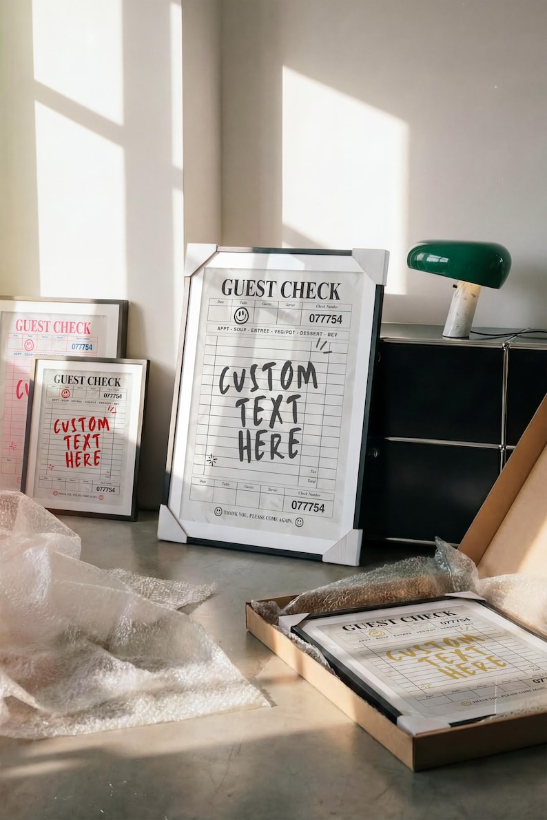 May include: Framed guest check art prints with the text "CUSTOM TEXT HERE" in various sizes. The prints feature a classic receipt design with the number 077754. One print is in a cardboard box, and another is on the floor.