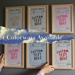 May include: Wooden framed prints of guest checks with the text "CUSTOM TEXT HERE" in various colors. The prints have a vintage aesthetic, with the words "GUEST CHECK" and the number "077754" at the top. The phrase "Other Colorways Available" is also visible.