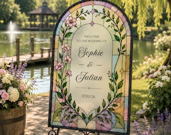 May include: An arched wedding welcome sign featuring a stained glass design with pink flowers and green vines. The center text reads: WELCOME TO THE WEDDING OF Sophie & Julian 07.03.26. The sign is held by a black metal stand with scrollwork details.