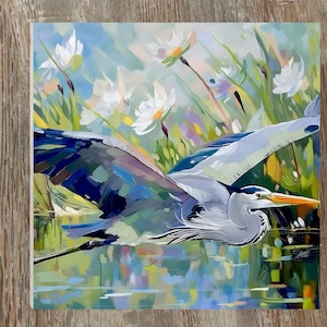 May include: An artistic painting of a great blue heron in flight over water. The bird's wings are spread, showcasing shades of blue, gray, and black. The background features white flowers and green foliage, with reflections in the water below.