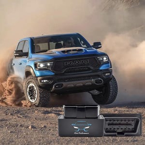 Può includere: Un pick-up blu solleva polvere mentre guida su una strada sterrata. In primo piano, un dispositivo nero con il testo "Fleet Performance" e un logo di un'auto, più un connettore OBD2 nero.