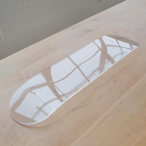 Puede incluir: Una bandeja de vidrio transparente y alargada con bordes redondeados. La bandeja refleja el patrón de una ventana, creando un juego de luces y sombras. Se encuentra sobre una superficie de madera clara.