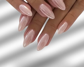 May include: Close-up of hands with long, almond-shaped nails painted in a pearlescent, light pink shade. The nails have a glossy finish. The hands are adorned with two silver rings, one with a row of small stones and another with three large, clear stones.
