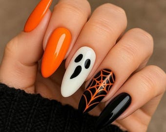 May include: Almond-shaped nails featuring a Halloween-themed manicure. The design includes solid bright orange nails, a white nail with a black ghost face, a black nail with an orange spiderweb pattern, and a solid glossy black nail.