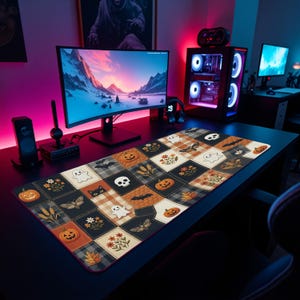 May include: A rectangular desk mat featuring a patchwork design of Halloween-themed squares. The pattern includes illustrations of orange pumpkins, white ghosts, black skulls, bats, moths, and autumn flowers on black, cream, and plaid backgrounds.