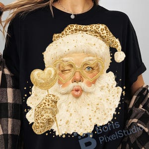 May include: Black t-shirt featuring a whimsical Santa Claus design. Santa is depicted winking, wearing heart-shaped glasses, and holding a gold heart-shaped lollipop. The Santa's hat and glove have a leopard print design.