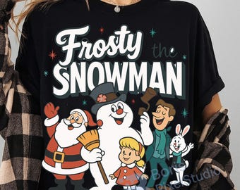 May include: Black t-shirt featuring the phrase "Frosty the Snowman" in white and green, with illustrations of Santa Claus, Frosty, a girl, and other characters. The design includes red and green accents.