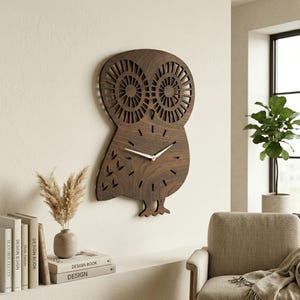 May include: A wooden owl-shaped wall clock with a dark brown finish. The clock features cut-out details for the eyes and feathers, and white clock hands. The clock is mounted on a light-colored wall.