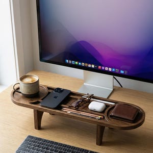 Könnte beinhalten: Ein brauner Schreibtisch-Organizer aus Holz mit integriertem Kaffeebecherhalter, Smartphone, Brille, Geldbörse und anderem Zubehör. Der Organizer befindet sich vor einem Computermonitor. Eine Tastatur ist im Vordergrund.