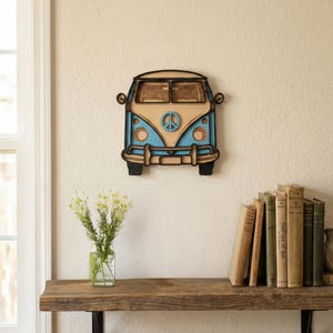Peut inclure: Décoration murale en bois représentant un van vintage bleu et beige avec un symbole de paix. Le van a des détails noirs et est monté sur un mur crème. Cet objet décoratif est idéal pour ajouter une touche rétro à une pièce.