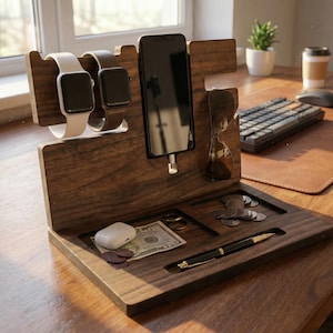 May include: A wooden desk organizer with slots for a smartphone, smartwatches, and sunglasses. It features a tray for small items like coins, a pen, and a pair of wireless earbuds. The organizer is made of dark wood.