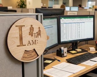 May include: A round, light-colored wooden sign with the text "I AM:" and a graphic of a person with a briefcase and another person sitting at a desk. The bottom of the sign reads "Wrestling with Spreadsheets".