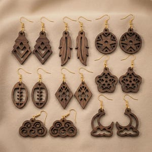 May include: A collection of wooden earrings with gold-colored hooks. The earrings feature various geometric and nature-inspired designs, including feathers, diamonds, stars, and moons. The earrings are a dark brown color.