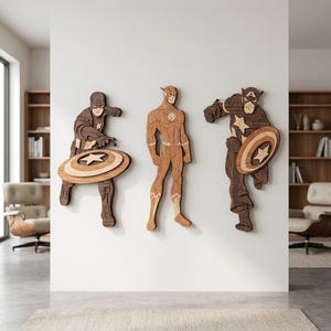 Puede incluir: Tres obras de arte mural de superhéroes de madera. Capitán América con escudo, The Flash y otra figura del Capitán América. Las figuras de madera son en tonos marrones y beige, montadas en una pared blanca. Los escudos del Capitán América tienen un diseño de estrella.